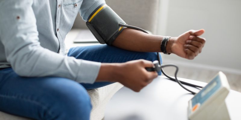 Unrecognizable African Guy Measuring Arterial Pressure Having Hypertension Indoor, Cropped