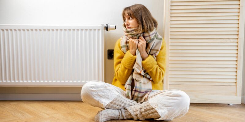 Warmly dressed woman near heater at home