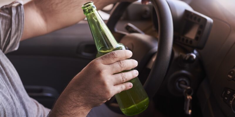 Bottle of beer in a man's hands driving the car during daytime