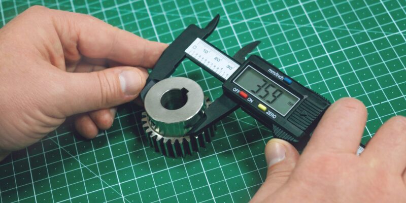 Metal gear measurement process. Factory man, worker measuring steel detail, gear with digital