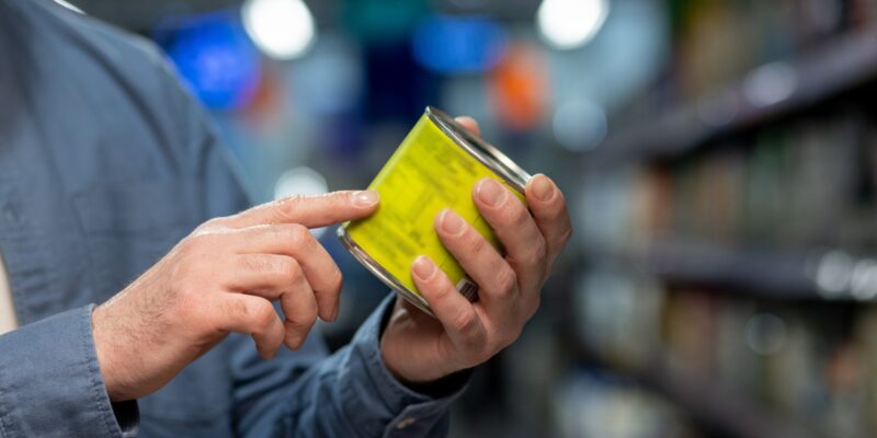 Close-up of person in grocery store examining product label on canned food with focus on details